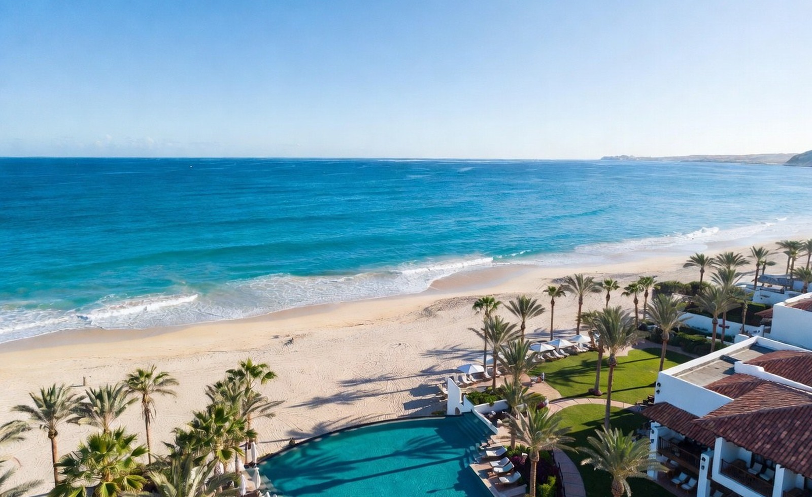 A bright resort beach with turquoise water, palms, and a pool terrace.
